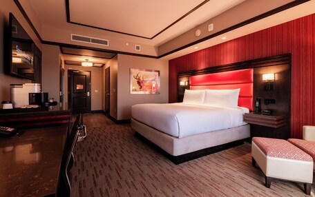A hotel room with a large bed, a desk with a computer, a chair, and a red accent wall.
