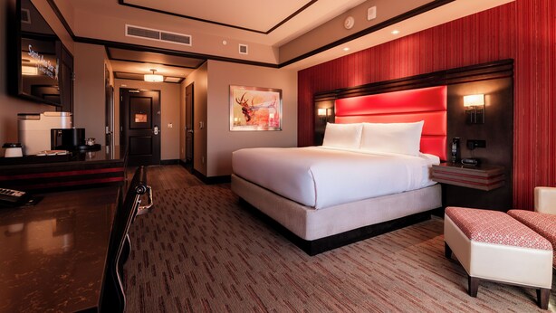 Una habitación de hotel con una cama grande, un escritorio con computadora, una silla y una pared decorada en rojo.