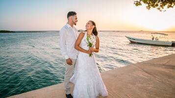 Una pareja está de pie junto al agua, con un barco al fondo.