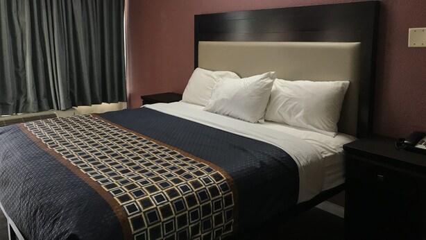 Ein Hotelzimmer mit einem Bett, einem Nachttisch, einem Telefon und einem Fenster mit Vorhängen.