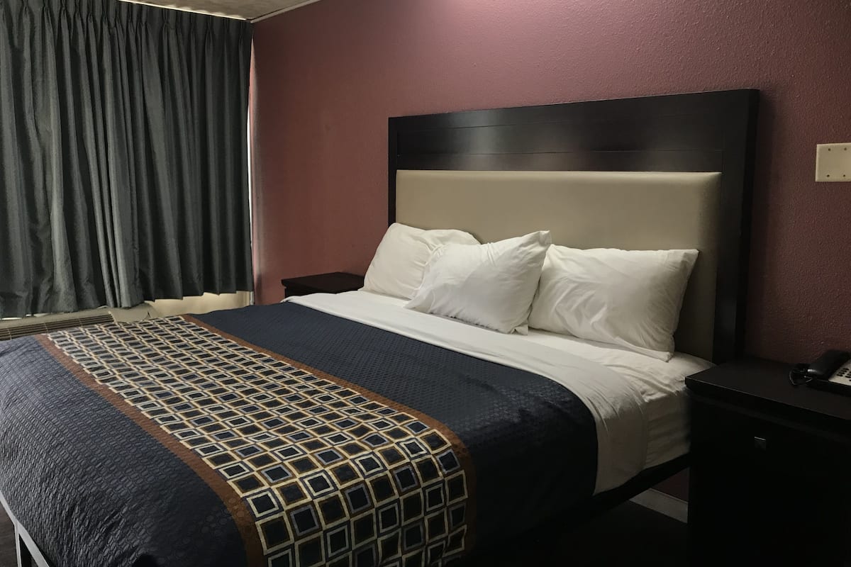 A hotel room with a bed, a nightstand, a telephone, and a window with curtains.