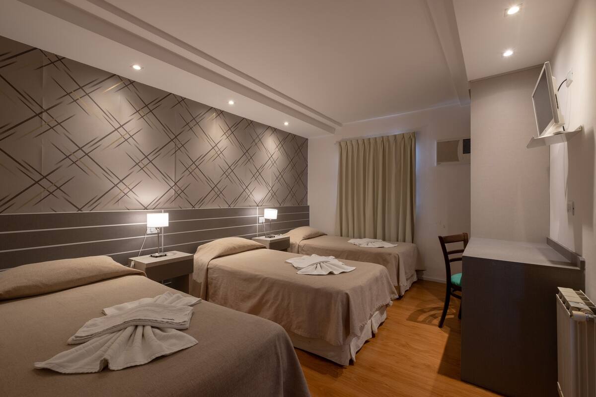 Una camera d'albergo con tre letti, una scrivania e uno specchio.