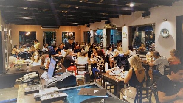 A busy restaurant with multiple dining tables and chairs, a reception desk with a phone and computer, and large windows allowing natural light. - Hotel La Posta (Oncativo)