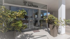 The entrance of Hotel La Posta with a glass facade, large potted plants, and a clear view of the interior through the glass doors. - Hotel La Posta (Oncativo)