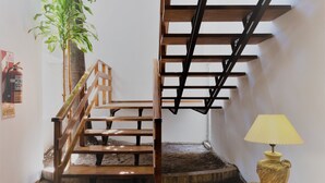 A wooden staircase with a handrail, a small round table with a lamp, and a potted plant. - Hotel La Posta (Oncativo)