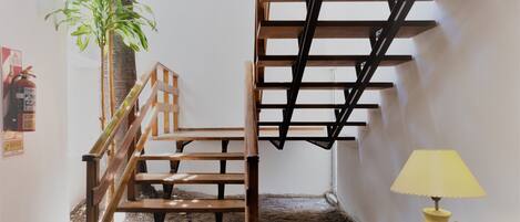 Una escalera de madera con barandilla, una mesita redonda con una lámpara y una planta en maceta.
