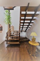 Una escalera de madera con barandilla, una mesita redonda con una lámpara y una planta en maceta.