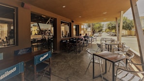 An outdoor cafe with tables and chairs, a wooden counter, and a view of the street. - Hotel La Posta (Oncativo)