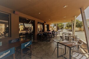 Un café al aire libre con mesas y sillas, una barra de madera y vistas a la calle.