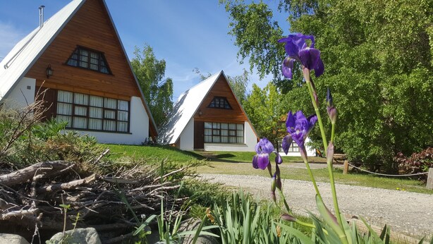 Une rangée de cabanes en bois aux toits en pente, entourées d’une végétation luxuriante et bordées d’un chemin de gravier.