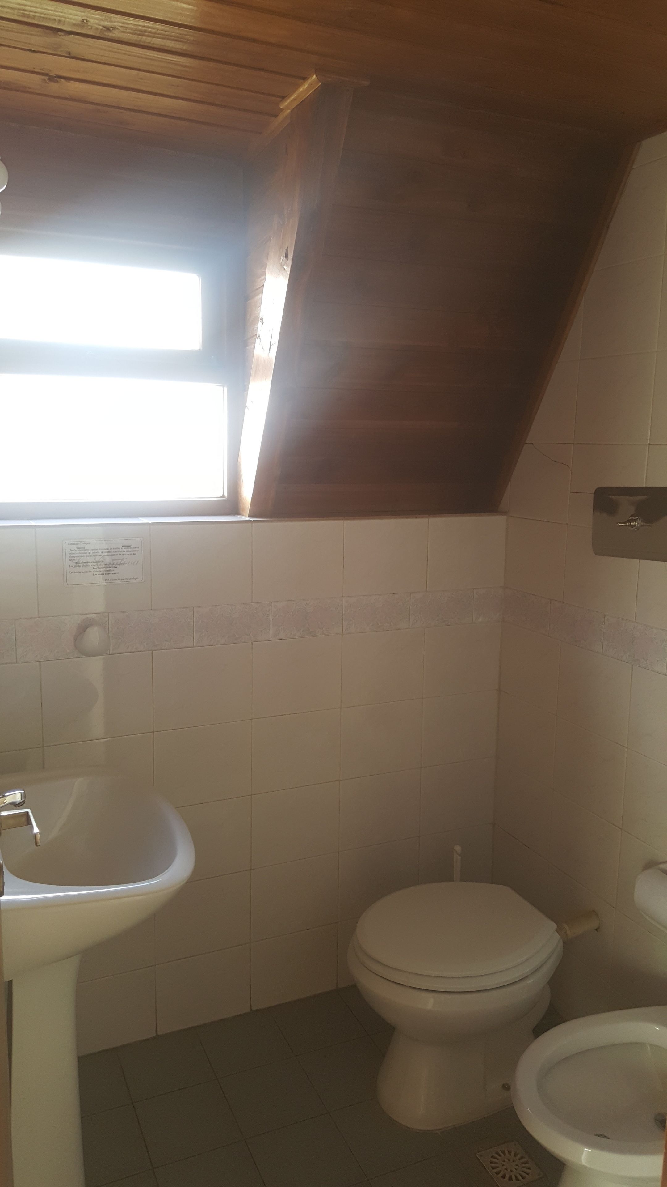 A bathroom with a sloped ceiling, a toilet, a sink, and a window allowing natural light.