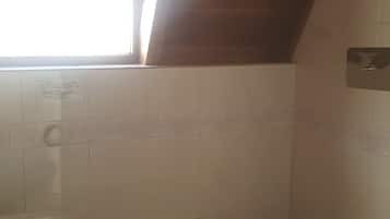 A bathroom with a sloped ceiling, a toilet, a sink, and a window allowing natural light.