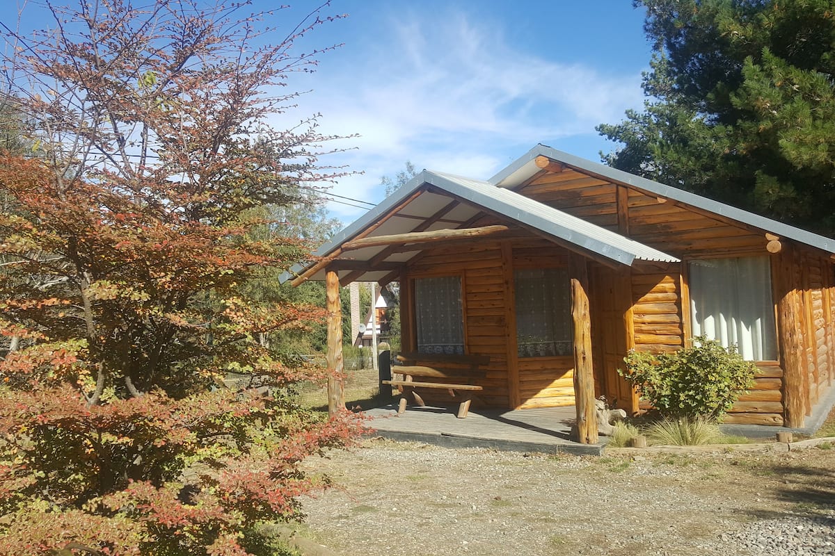 Ein kleines Blockhaus mit Veranda, umgeben von Bäumen im Herbstlaub.