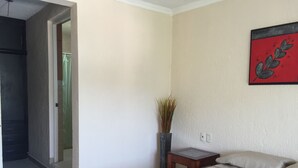 Quarto de hotel com uma cama, uma mesa pequena, um vaso com plantas e um quadro na parede.