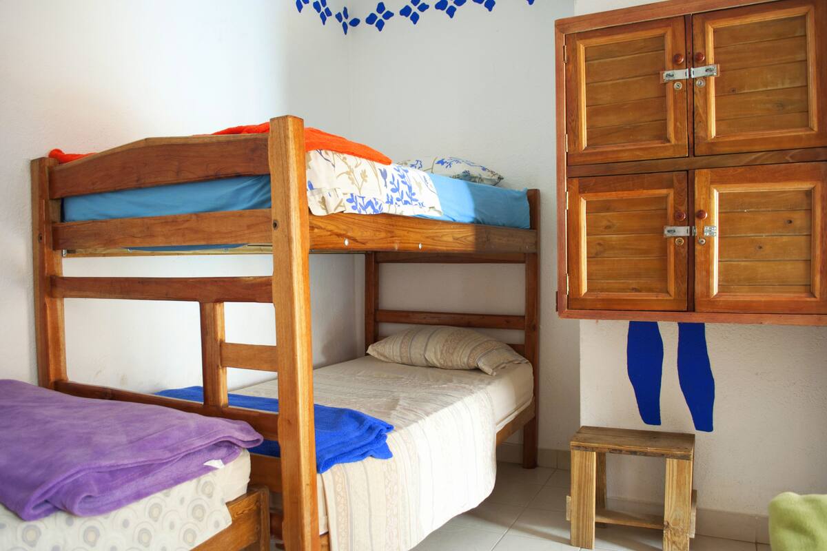 Un lit superposé avec une structure en bois, un petit tabouret en bois et une armoire à deux portes.
