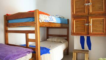 Una cama individual con estructura de madera, un taburete pequeño de madera y un armario con dos puertas.