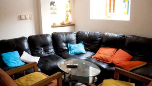 A living room with a black leather sectional sofa, a glass coffee table, and wooden chairs.