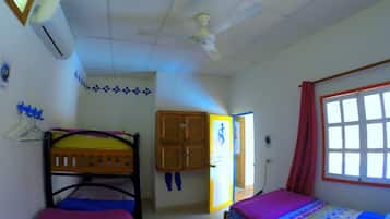 Quarto com beliches, ventilador de teto, ar condicionado, janela com cortinas e porta que dá para outro cômodo.