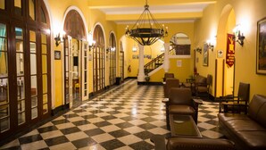 A hotel lobby with a checkered floor, wooden doors, a staircase, and seating areas.