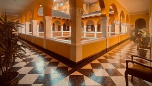 A hotel corridor with checkered flooring, arched alcoves, and potted plants.