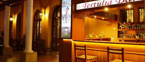 A bar named 'Tertulia Bar' with wooden bar stools, a tiled floor, and a warm interior ambiance.