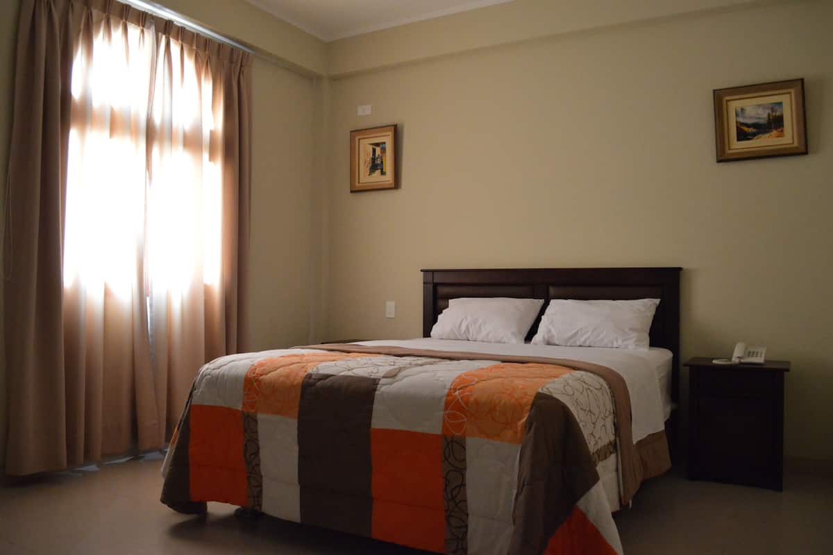 Une chambre d’hôtel avec un lit, une table de chevet, un téléphone et deux tableaux encadrés au mur.
