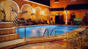 An indoor swimming pool with a stone wall, metal railings, and potted plants.
