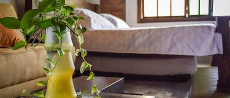 Una sala de estar con sofá, una mesita de centro con una planta y una revista, y una cama al fondo.