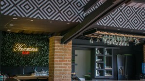 A bar area with a neon sign reading "Nostalgia BAR," a brick pillar, hanging glassware, and a bar counter with stools.
