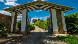 An entrance with a covered walkway leading to a gate, surrounded by greenery and a clear sky.