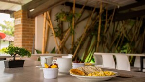 A breakfast table with a plate of scrambled eggs, toast, and fruit, white cups, and a small potted plant.