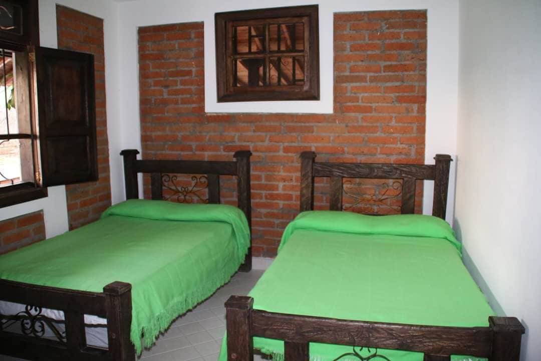 Una habitación con dos camas de madera, ropa de cama verde, una pared de ladrillo y una ventana con marco de madera.