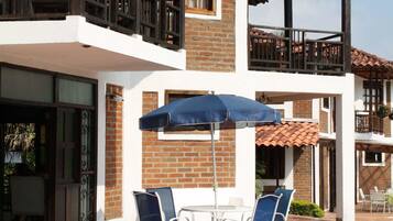 A two-story building with a patio area featuring a table and chairs under a blue umbrella.