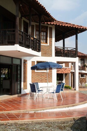 A two-story building with a patio area featuring a table and chairs under a blue umbrella. - Villa Manuela - Finca Hotel Casa Nostra (Quimbaya)