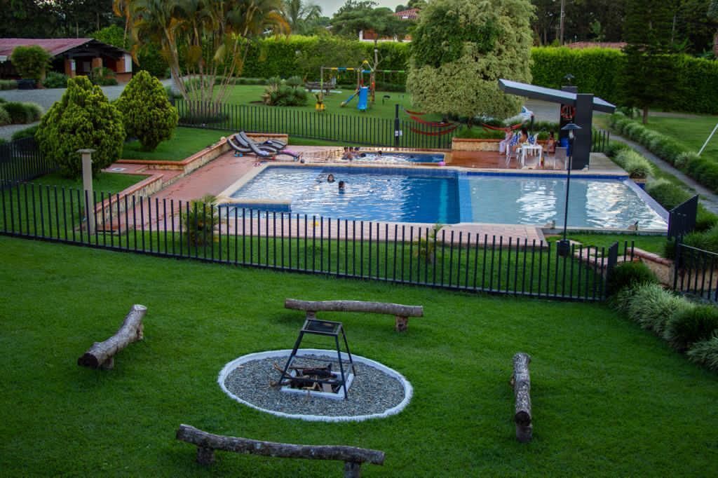 A swimming pool surrounded by a fence, with a grassy area and a swing set in the background.