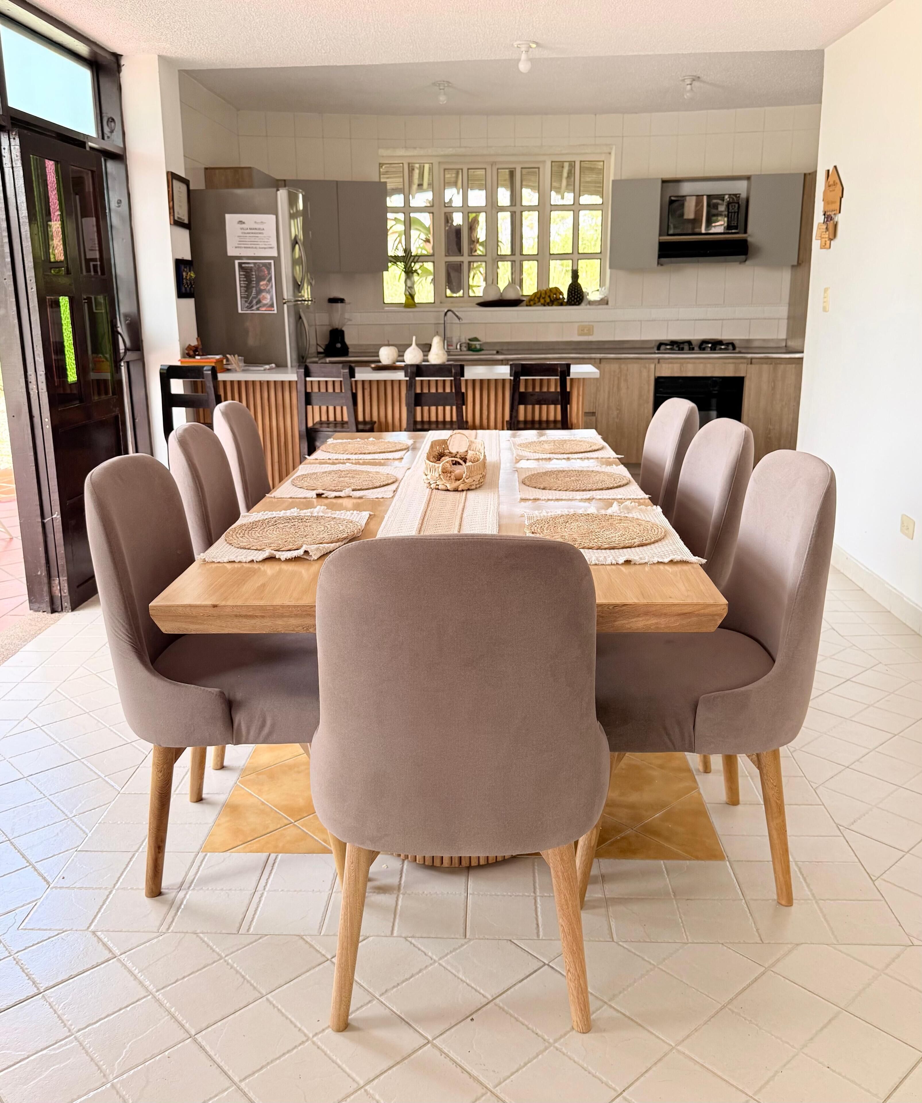 A dining area with a long wooden table, six upholstered chairs, and woven placemats.