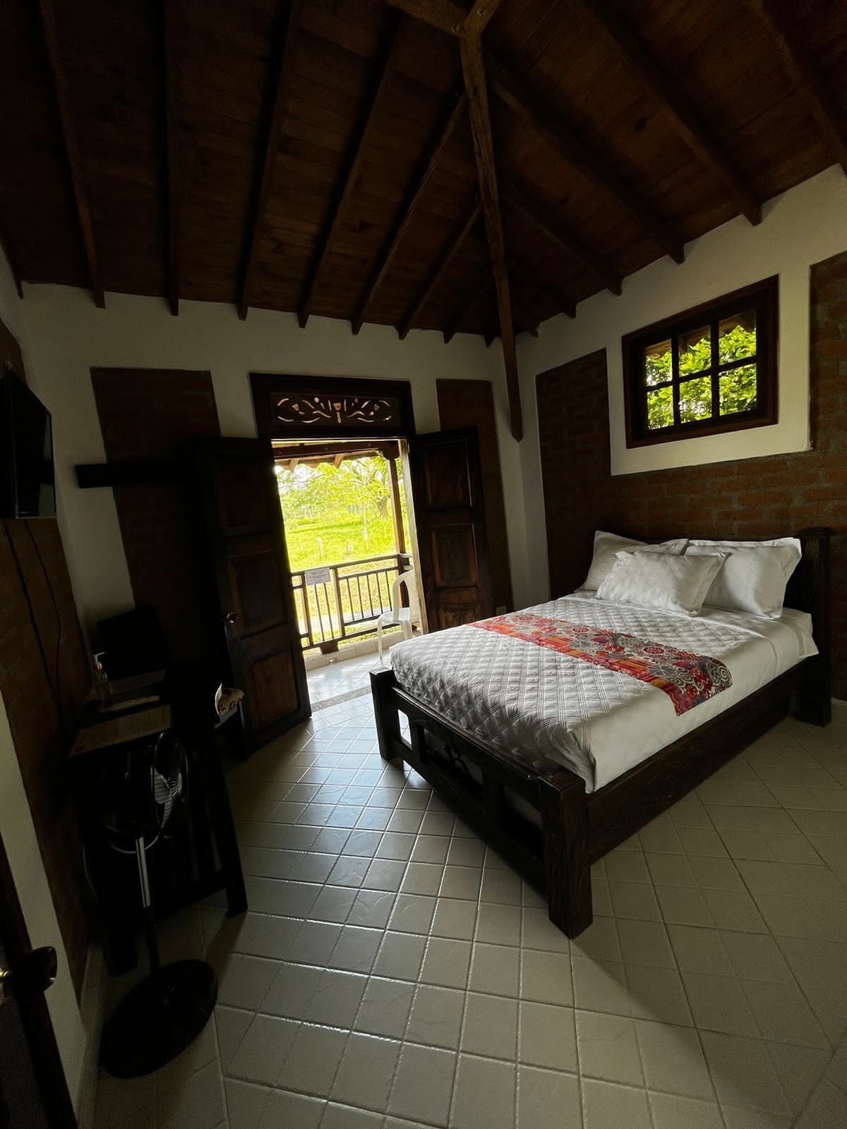 A bedroom with a bed, a wooden ceiling, a window, and a door leading outside.