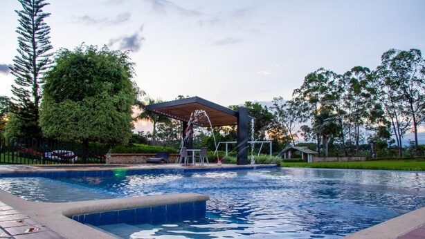 A swimming pool with a wooden deck, surrounded by trees and a covered seating area.