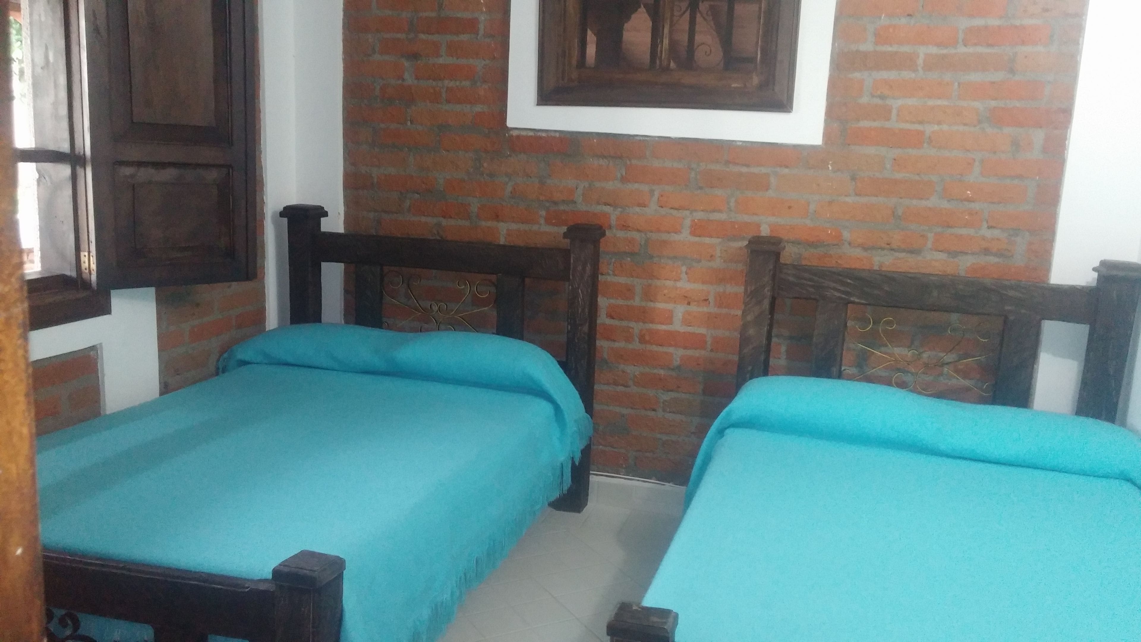 A room with two beds, a brick wall, and a framed picture on the wall.
