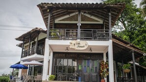 A two-story building with a balcony, a sign reading "Villa Manuel," outdoor seating with umbrellas, and a potted plant.