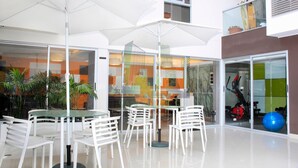Espaço moderno em ambiente interno, com paredes de vidro, móveis brancos e equipamentos de ginástica.