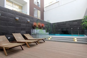 Un espace aménagé au bord de la piscine, avec des chaises longues en bois, un mur en pierre et une barrière en verre.