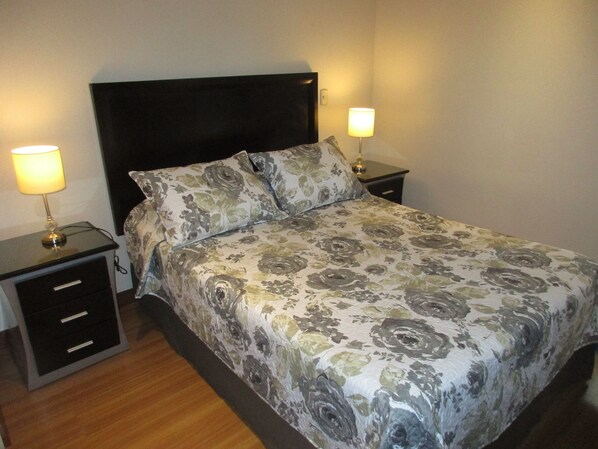 A neatly made bed with floral bedding, two bedside tables with lamps, and a dark headboard.