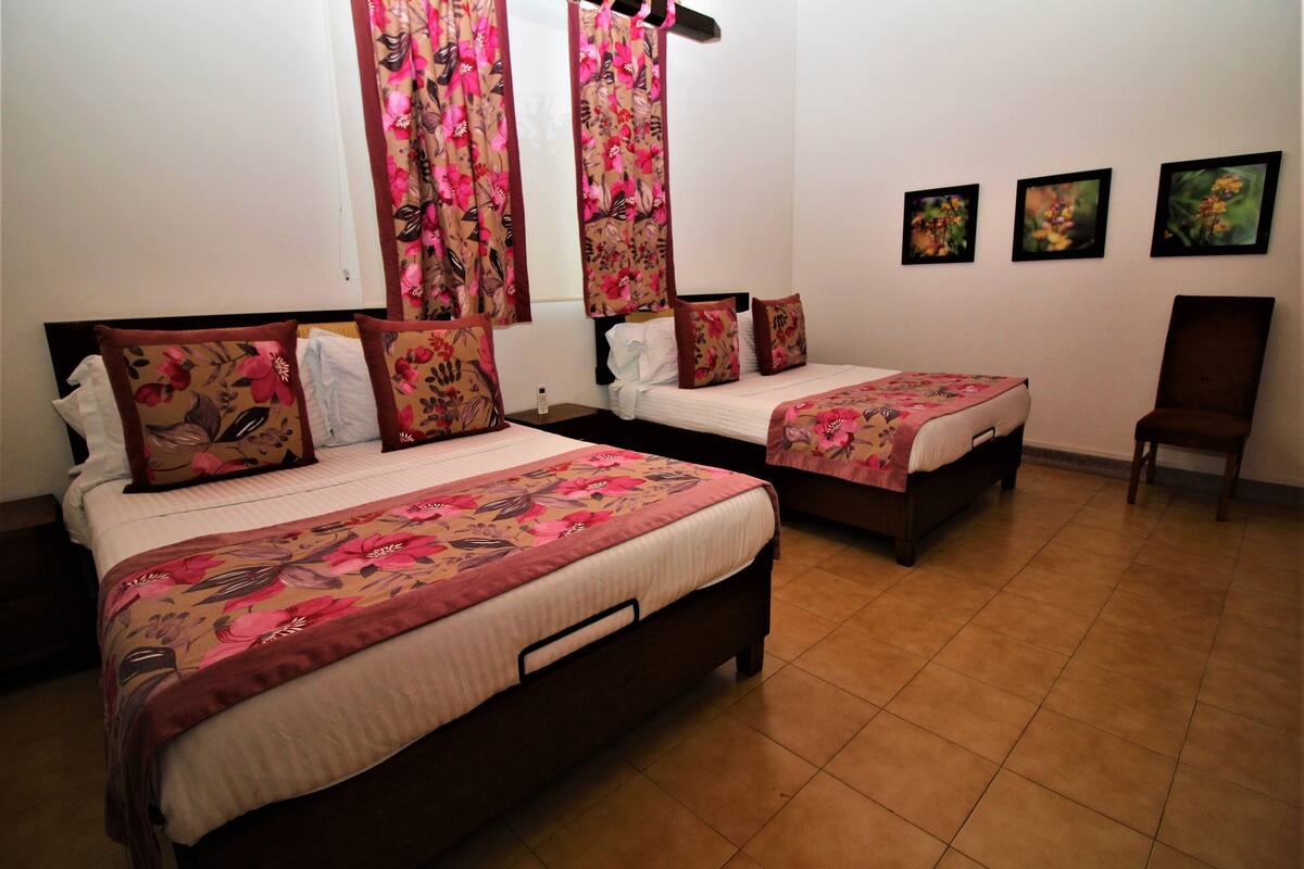 Een hotelkamer met twee bedden, bloemenbedekkers, een houten stoel en drie ingelijste kunstwerken aan de muur.