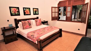 A bedroom with a wooden bed, a nightstand, a dresser, and a window with an open shutter. - Amazilia Hotel (Pereira)