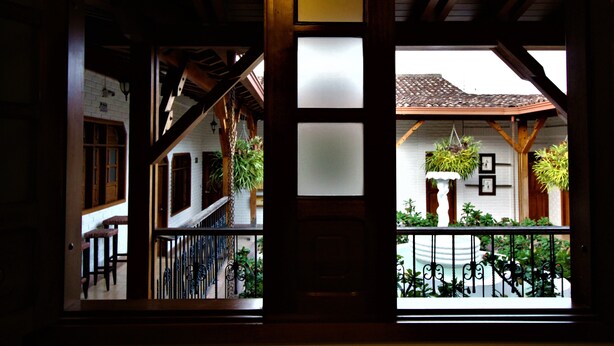 A view through a wooden-framed window with a balcony, featuring a tiled roof and potted plants. - Amazilia Hotel (Pereira)