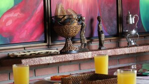 A breakfast setting with a fruit painting, a basket of bread, a sugar bowl, and two glasses of orange juice. - Amazilia Hotel (Pereira)