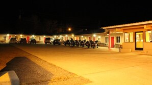 Ein Motel mit mehreren Zimmern, jedes mit einer roten Tür, und mehreren parkenden Autos und Motorrädern auf dem Parkplatz.