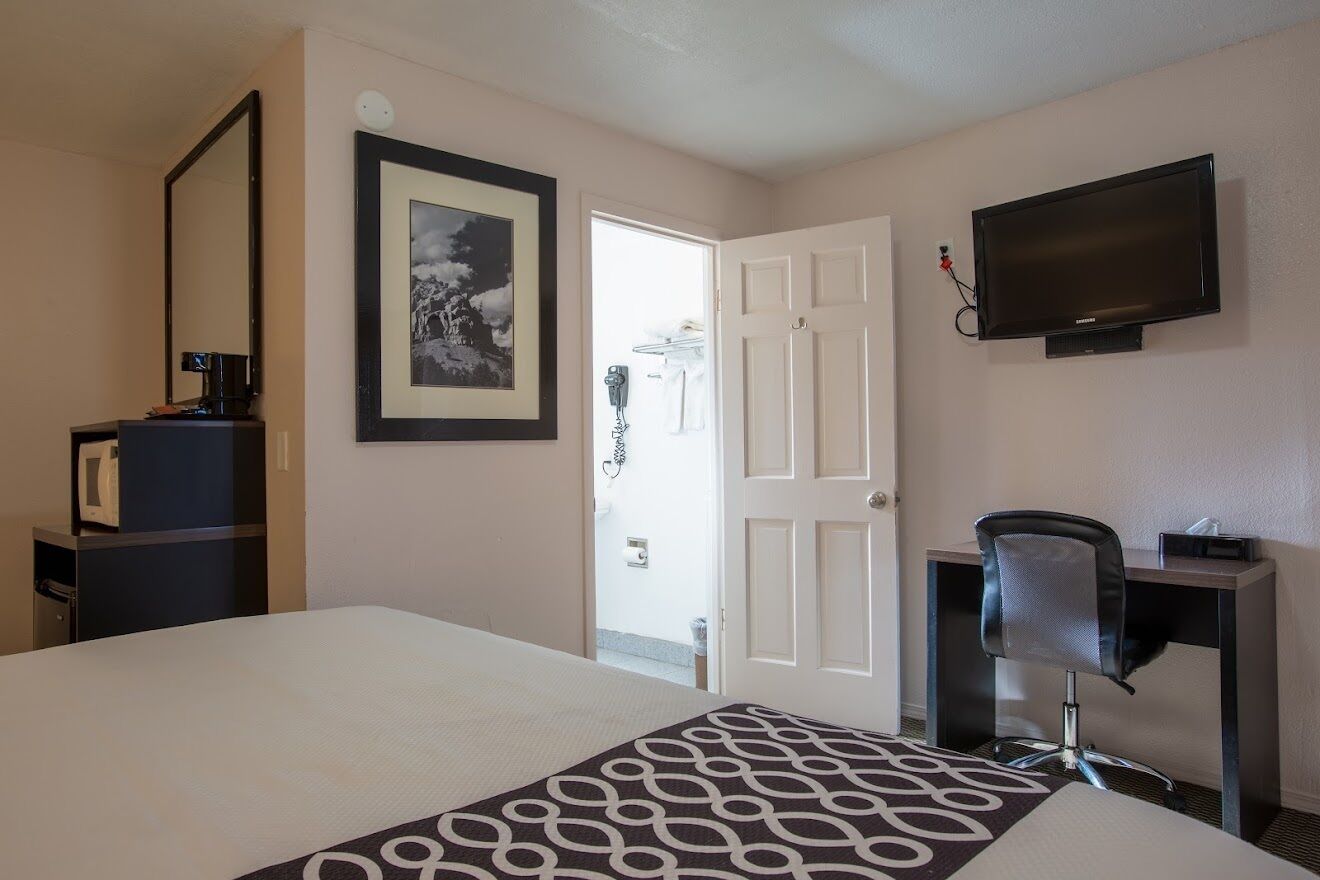 A hotel room with a bed, a desk, a chair, a television, a framed picture, and a door leading to a bathroom.
