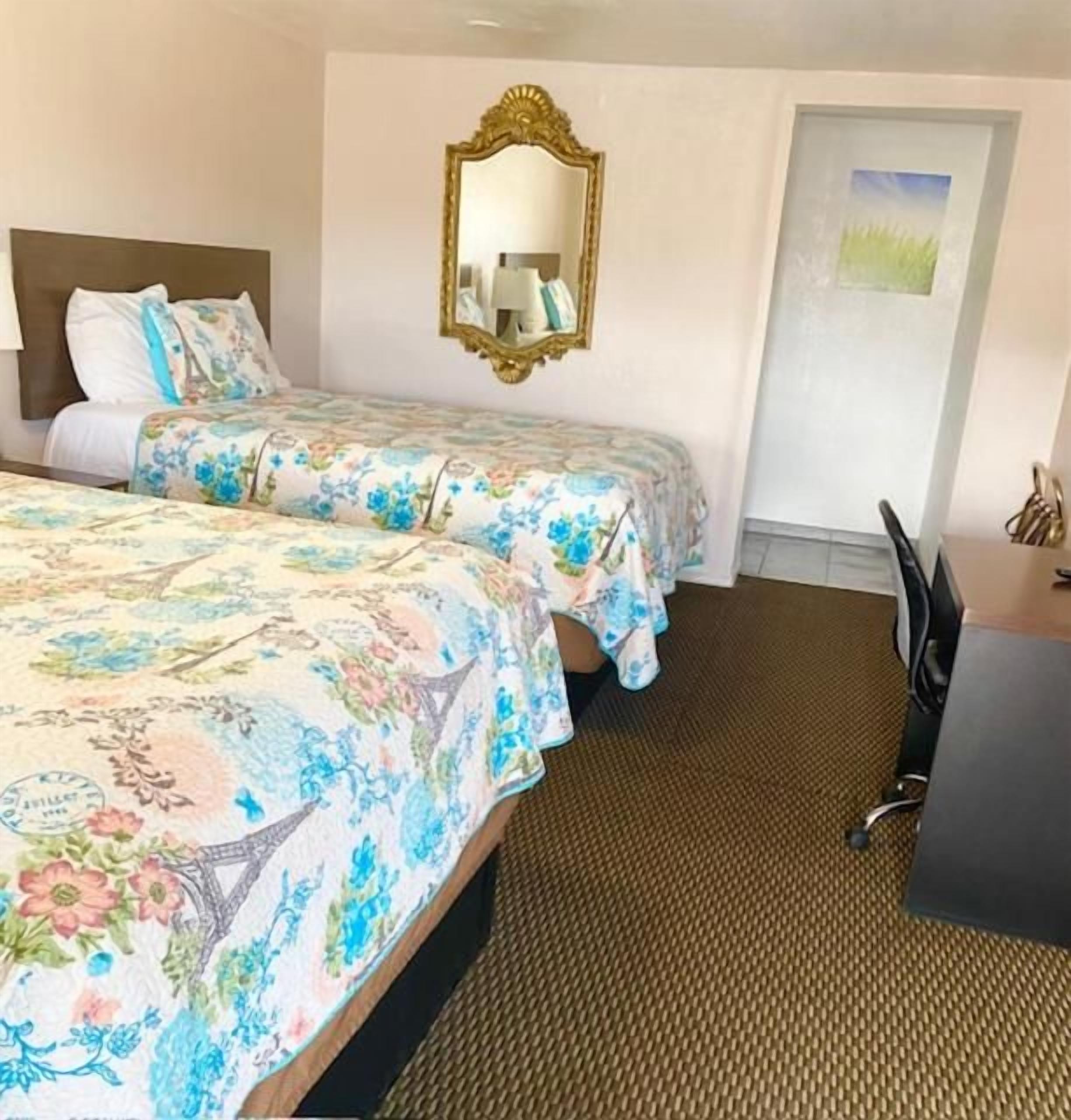 A hotel room with two beds, a mirror, a desk, and a chair.